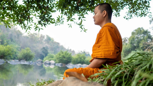 Monk meditating peacefully beside serene mountain lake representing mindfulness, spiritual practice, and inner peace cultivation